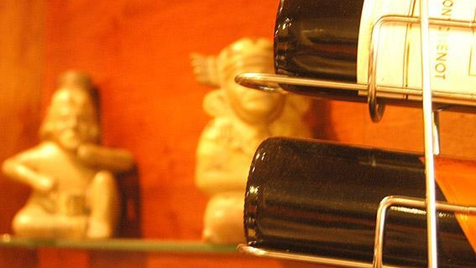 Botellas de vino de cerca con huacos peruanos desenfocados detrás.